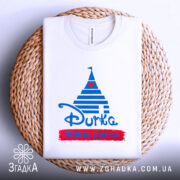 Футболка повна дурка, біла футболка з коротким рукавом, складена на плетеній кошику, фон світло-сірий, принт у вигляді синіх смуг з червоним написом 'ПОВНА ДУРКА' та синьою пірамідою.