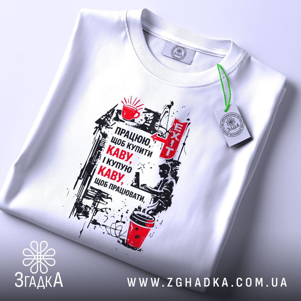 Футболка працюю за каву, білого кольору, зображена зверху, фон світло-сірий, принт з текстом про каву та малюнком, на футболці є етикетка з зеленим шнурком.