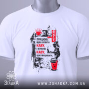 Футболка працюю за каву, білого кольору, зображена зверху, фон світло-сірий, принт з текстом про каву та малюнком, на футболці є етикетка з зеленим шнурком.