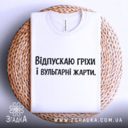 Футболка провокаційний напис, складена біла футболка, зображена зверху на плетеній основі, фон світло-сірий, принт чорного кольору з текстом "Відпускаю гріхи і вульгарні жарти".