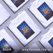 Футболка Пиздьож Пікчерз білого кольору, зображена з фронтального ракурсу на манекені, фон світло-сірий, принт з написом на синьому фоні з променями, зображення гір на нижній частині принта.