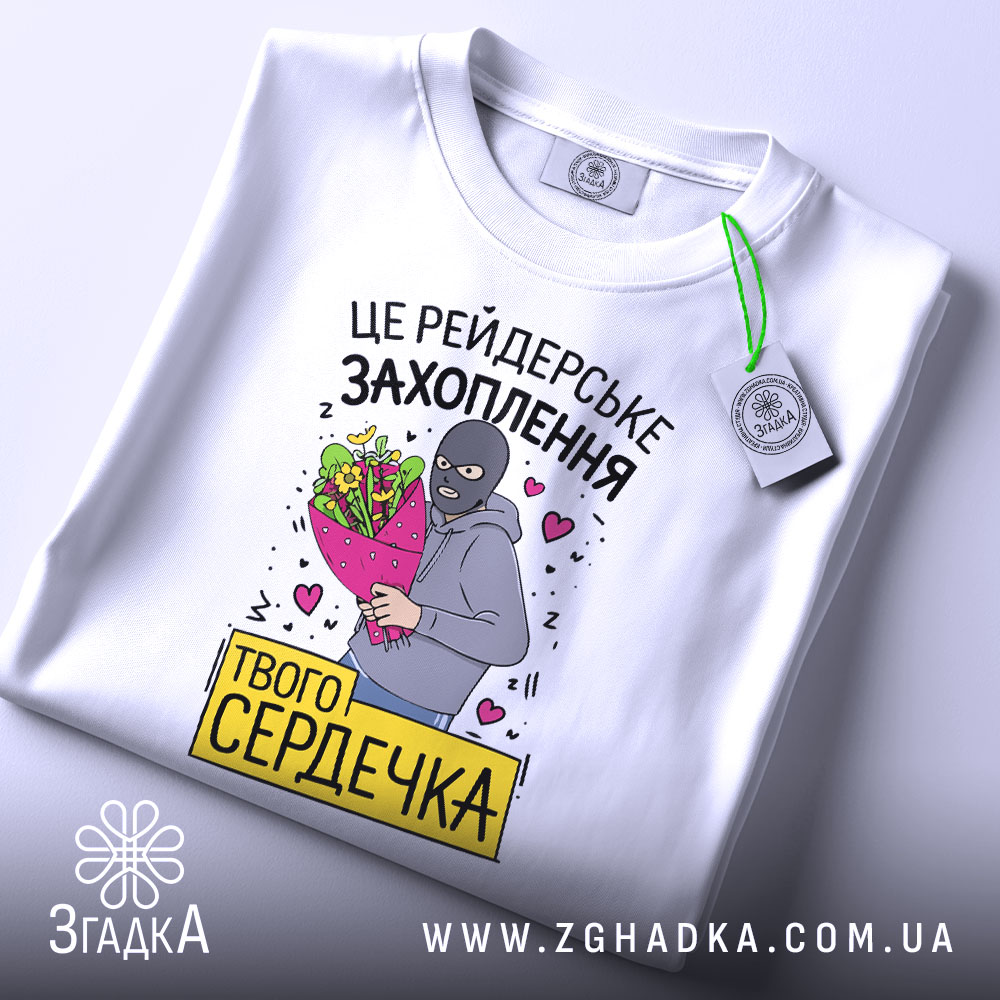 Футболка рейдерське захоплення, біла, складена на поверхні, фон світло-сірий, принт з малюнком людини в масці з букетом квітів та написом, з етикеткою.