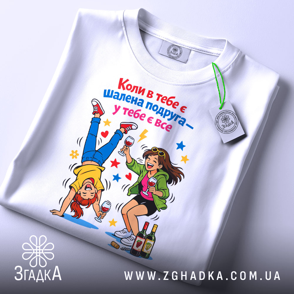 Футболка шалена подруга завжди білого кольору, зображена з верхнього ракурсу, на фоні світло-сірого кольору. Принт показує двох дівчат, одна з яких стоїть на руках, а інша тримає келих, з яскравими зірочками навколо.