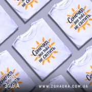 Футболка сонечко не світить. Біла футболка з коротким рукавом, зображена з фронтального ракурсу на манекені, фон світло-сірий, принт з написом "Сонечко, яке тобі не світить" оранжевого кольору з жовтими променями.