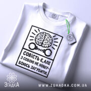 Футболка совість є білого кольору, складена на столі, фон світло-сірий, принт чорного кольору з малюнком мозку та наручниками, текст українською мовою, на комірці видна етикетка.