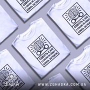 Футболка совість є білого кольору, зображена на манекені, фон світло-сірий, принт чорного кольору з малюнком мозку та наручниками, текст українською мовою.