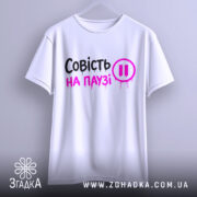 Футболка совість на паузі, білого кольору, підвішена на вішалці, фон світло-сірий, принт чорного та рожевого кольорів з написом 'Совість на паузі' і символом паузи.