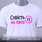 Футболка совість на паузі, білого кольору, складена на поверхні, фон світло-сірий, принт чорного та рожевого кольорів з написом 'Совість на паузі' і символом паузи, з етикеткою на рукаві.