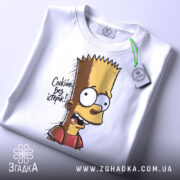 Футболка спокійно без істерик, складена на поверхні, фон світлий, принт з Бартом Симпсоном, текст 'Спокійно без істерик', на футболці присутня етикетка з зеленим шнурком.