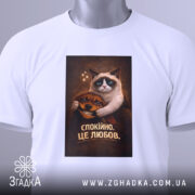 Футболка спокійно це любов. Біла футболка, складена на поверхні, з принтом кота і собаки, фон світлий, присутня етикетка з зеленим шнурком.