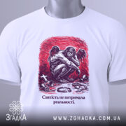 Футболка святість і реальність. Біла футболка з коротким рукавом, зображена з верхнього ракурсу на фоні світлого кольору. На футболці принт з зображенням ангела, що сидить, з червоним фоном. На футболці також видно етикетку з логотипом бренду.