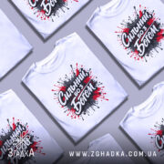 Футболка сильний з Богом, біла, зображена на манекені, фон світло-сірий, принт з червоними та чорними краплями фарби навколо напису 'Сильний, бо з Богом'.