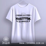 Футболка тримаю себе в руках, білого кольору, з фронтального ракурсу, підвішена на вішалці, фон світло-сірий, принт чорного кольору з текстом та графічними елементами.