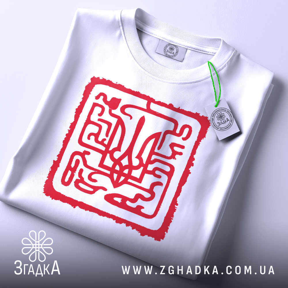 Футболка тризуб код нації, біла, складена на столі, фон світло-сірий, принт червоний з абстрактним тризубом, на комірці є етикетка з зеленим шнурком.