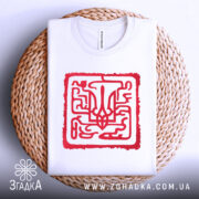 Футболка тризуб код нації, біла, складена на плетеному кошику, фон світло-сірий, принт червоний з абстрактним тризубом, видно комірець.