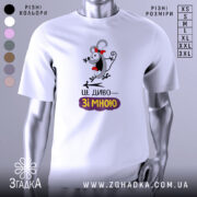 Футболка це диво. Біла футболка з коротким рукавом, зображена з фронтального ракурсу на манекені. На футболці яскравий принт з веселим персонажем, який має червону стрічку на голові, а під ним напис "ЦЕ ДИВО—ЗІ МНОЮ". Фон нейтральний, з легким градієнтом.