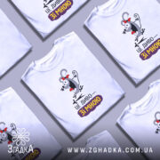 Футболка це диво. Біла футболка з коротким рукавом, зображена з фронтального ракурсу на манекені. На футболці яскравий принт з веселим персонажем, який має червону стрічку на голові, а під ним напис "ЦЕ ДИВО—ЗІ МНОЮ". Фон нейтральний, з легким градієнтом.