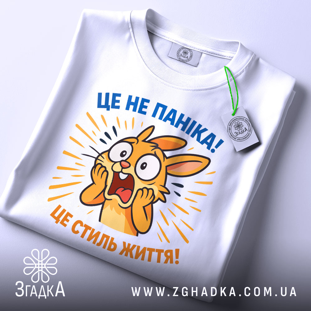 Футболка це не паніка. Біла футболка з принтом, на якому зображено переляканого кролика, що кричить. Принт яскравий, з жовтими та синіми елементами, на фоні світло-сірого кольору. Футболка зображена зверху, з етикеткою, що звисає.