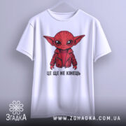 Футболка це ще не кінець. Біла футболка з принтом червоного персонажа в червоній куртці, зображена з фронтального ракурсу на нейтральному фоні. Текст "ЦЕ ЩЕ НЕ КІНЕЦЬ" розташований під принтом.