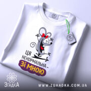 Футболка ця ненормальна. Білий колір, зображена з верхнього ракурсу, фон світло-сірий, принт з мишкою, що сміється, з червоною стрічкою, текст "Ця ненормальна – зі мною" під малюнком, на комірці видно етикетку.