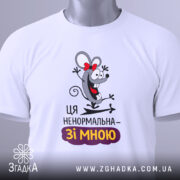 Футболка ця ненормальна. Білий колір, зображена з верхнього ракурсу, фон світло-сірий, принт з мишкою, що сміється, з червоною стрічкою, текст "Ця ненормальна – зі мною" під малюнком, на комірці видно етикетку.