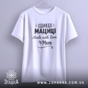 Футболка Циці Мациці білого кольору, підвішена на вішалці, фон світло-сірий, принт чорного кольору з написом 'Циці Мациці Made with love by Mom'.