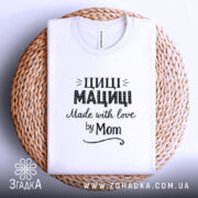 Футболка Циці Мациці білого кольору, складена на плетеній основі, фон світло-сірий, принт чорного кольору з написом 'Циці Мациці Made with love by Mom'.