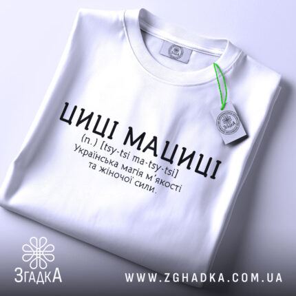 Футболка циці мациці білого кольору, складена на поверхні, фон світлий, принт чорного кольору з текстом про українську магію жіночої сили, на комірці видна етикетка.