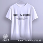 Футболка циці мациці білого кольору, підвішена на вішалці, фон світлий, принт чорного кольору з текстом про українську магію жіночої сили.