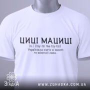 Футболка циці мациці білого кольору, складена на поверхні, фон світлий, принт чорного кольору з текстом про українську магію жіночої сили, на комірці видна етикетка.