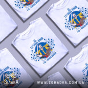 Футболка тут наша земля. Біла футболка з коротким рукавом, зображена з правого ракурсу на манекені. На фоні світло-сірий колір. Принт зображає чоловіка з мечем та щитом, оточеного декоративними елементами у синьому та жовтому кольорах.