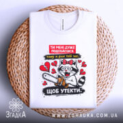 Футболка ти мені подобаєшся. Біла футболка, складена на плетеній основі, з принтом кота з бензопилою, фон натуральний, текстурований.