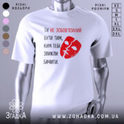 Футболка ти не зобов’язаний білого кольору, з принтом червоного кольору у вигляді маски та текстом, розташована на манекені, фон нейтральний, з легким градієнтом.