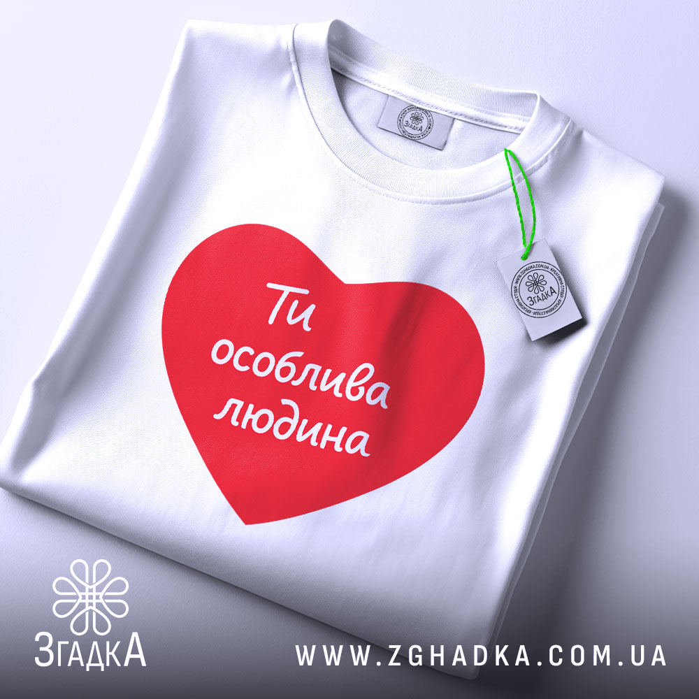 Футболка ти особлива людина. Біла футболка з червоним принтом у формі серця, на якому написано 'Ти особлива людина'. Футболка складена на білому фоні, з видимим етикеткою.