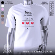 Футболка ти переміг, біла футболка з принтом, зображена з близького ракурсу, фон нейтральний, на футболці чорний текст і червоні сердечка на ігровому полі.