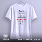 Футболка ти переміг, біла футболка підвішена на вішалці, фон світлий, принт з чорним текстом і червоними сердечками, зображена з фронтального ракурсу.