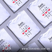 Футболка ти переміг, біла футболка з принтом, зображена з близького ракурсу, фон нейтральний, на футболці чорний текст і червоні сердечка на ігровому полі.