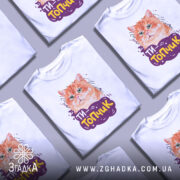 Футболка ти топчик, біла, зображена на манекені, фон світло-сірий, принт з оранжевим котом та написом 'ТИ-Топчик' у фіолетовій обгортці.