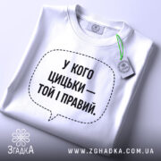 Футболка у кого цицьки, білого кольору, зображена зверху на столі, фон світло-сірий, принт чорного кольору з текстом у формі діалогового вікна, на комірці видна етикетка.