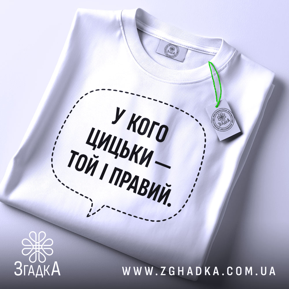 Футболка у кого цицьки, білого кольору, зображена зверху на столі, фон світло-сірий, принт чорного кольору з текстом у формі діалогового вікна, на комірці видна етикетка.