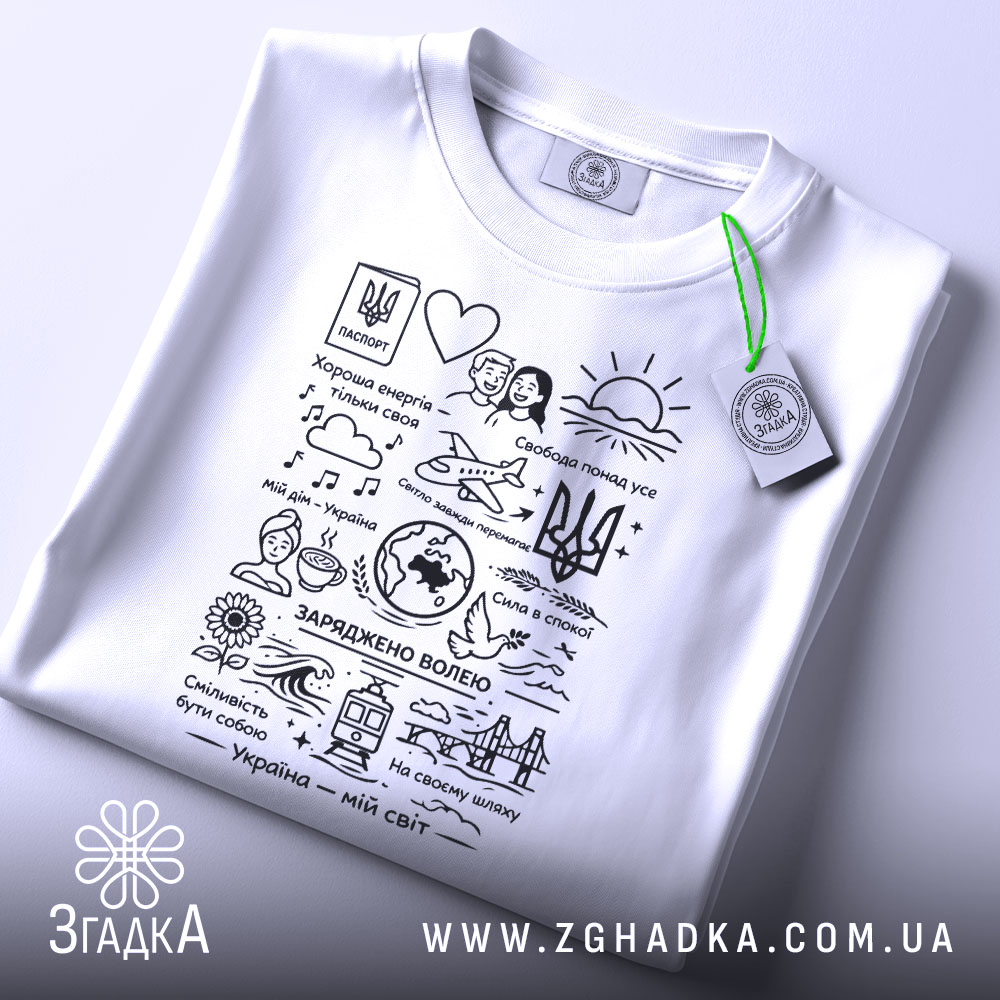 Футболка Україна мій світ, біла, складена на поверхні, фон світлий, принт чорного кольору з малюнками та текстами, на футболці є зелений ярлик.