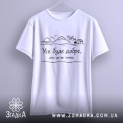 Футболка усе буде добре, на білому фоні, підвішена на вішалці, з фронтального ракурсу, принт з пейзажем та текстом чорного кольору.