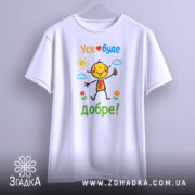 Футболка усе буде добре. Біла футболка, підвішена на вішалці, з кольоровим принтом усміхненого персонажа, текстом 'Усе❤️буде добре!' та елементами природи на фоні.