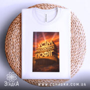 Футболка усім абсолютно пофіг. Біла футболка, зображена на плетеній кошику, принт з написом 'УСІМ АБСОЛЮТНО ПОФІГ', фон світлий, футболка акуратно складена.