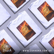 Футболка усім абсолютно пофіг. Біла футболка з принтом, зображення розташоване по центру, фон з градієнтом від світло-сірого до білого, принт з написом 'УСІМ АБСОЛЮТНО ПОФІГ' на фоні з оранжевими та жовтими відтінками.