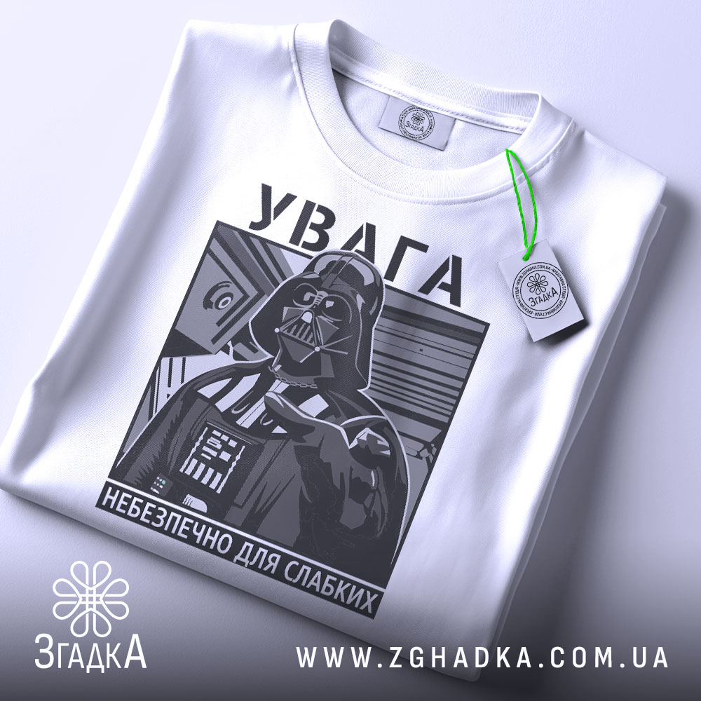 Футболка увага небезпечно, біла, зображена зверху, фон світлий, принт з зображенням персонажа в чорному кольорі, на комірці є етикетка.