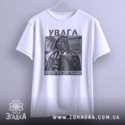 Футболка увага небезпечно, біла, зображена з фронтального ракурсу, фон світло-сірий, принт з зображенням персонажа в чорному кольорі з текстом на українській мові.