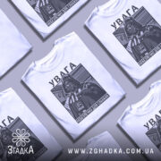 Футболка увага небезпечно, біла, зображена з фронтального ракурсу, фон нейтральний, принт з зображенням персонажа в чорному кольорі з текстом на українській мові.