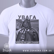 Футболка увага небезпечно, біла, зображена зверху, фон світлий, принт з зображенням персонажа в чорному кольорі, на комірці є етикетка.