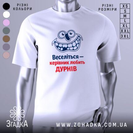Футболка веселий керівник. Біла футболка, зображена з фронтального ракурсу на манекені, фон світло-сірий. Принт з усміхненим персонажем та текстом "Веселіться — керівник любить ДУРНІВ" у синьому та червоному кольорах.